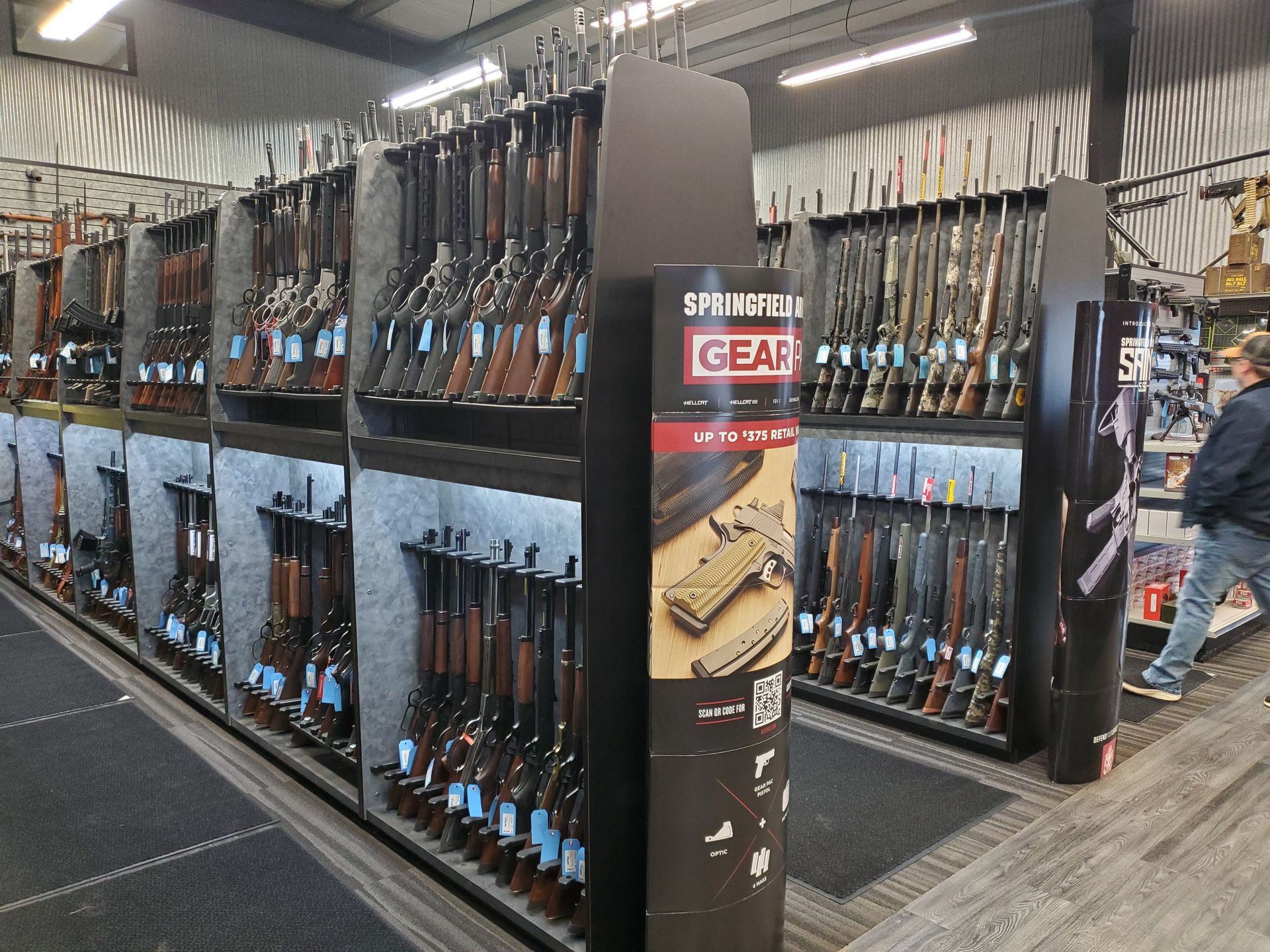 Interior of a gun store with rifles on display; aisles with shelves of merchandise and a doorway.