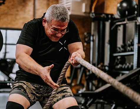 Man in black shirt and camo shorts pulling battle ropes in a gym