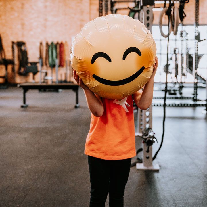 Person in an orange shirt holding a large smiley balloon in a gym