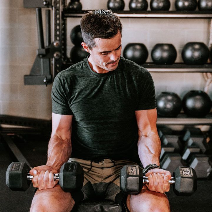 Man lifting dumbbells in a gym, looking down with a focused expression