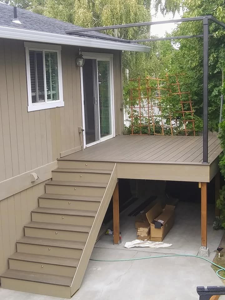 Backyard deck with stairs leading up, tan siding, and overhead pergola.