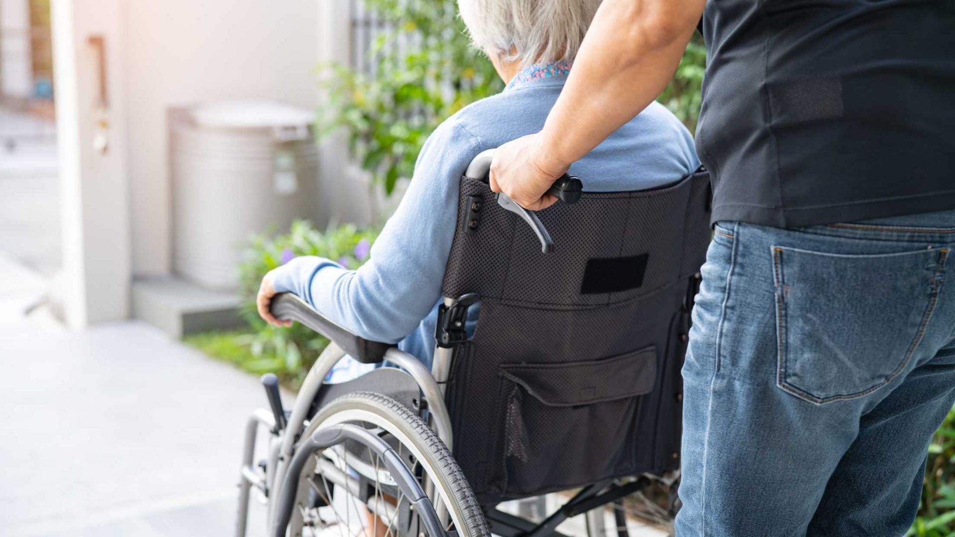 person pushing an elderly person in a wheelchair outside