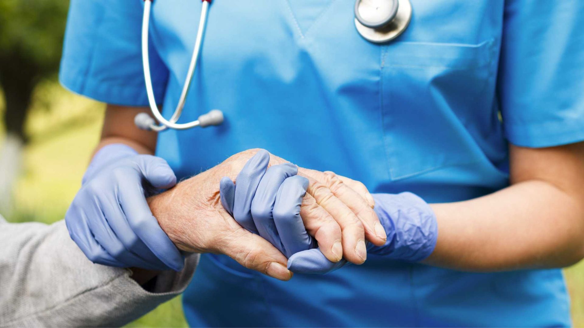 A nurse is holding the hand of an elderly woman.