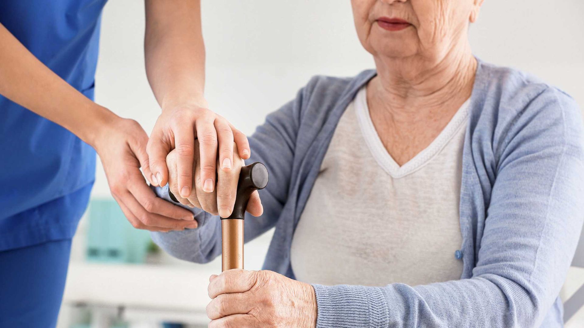 A nurse is helping an elderly woman in a wheelchair with a cane.