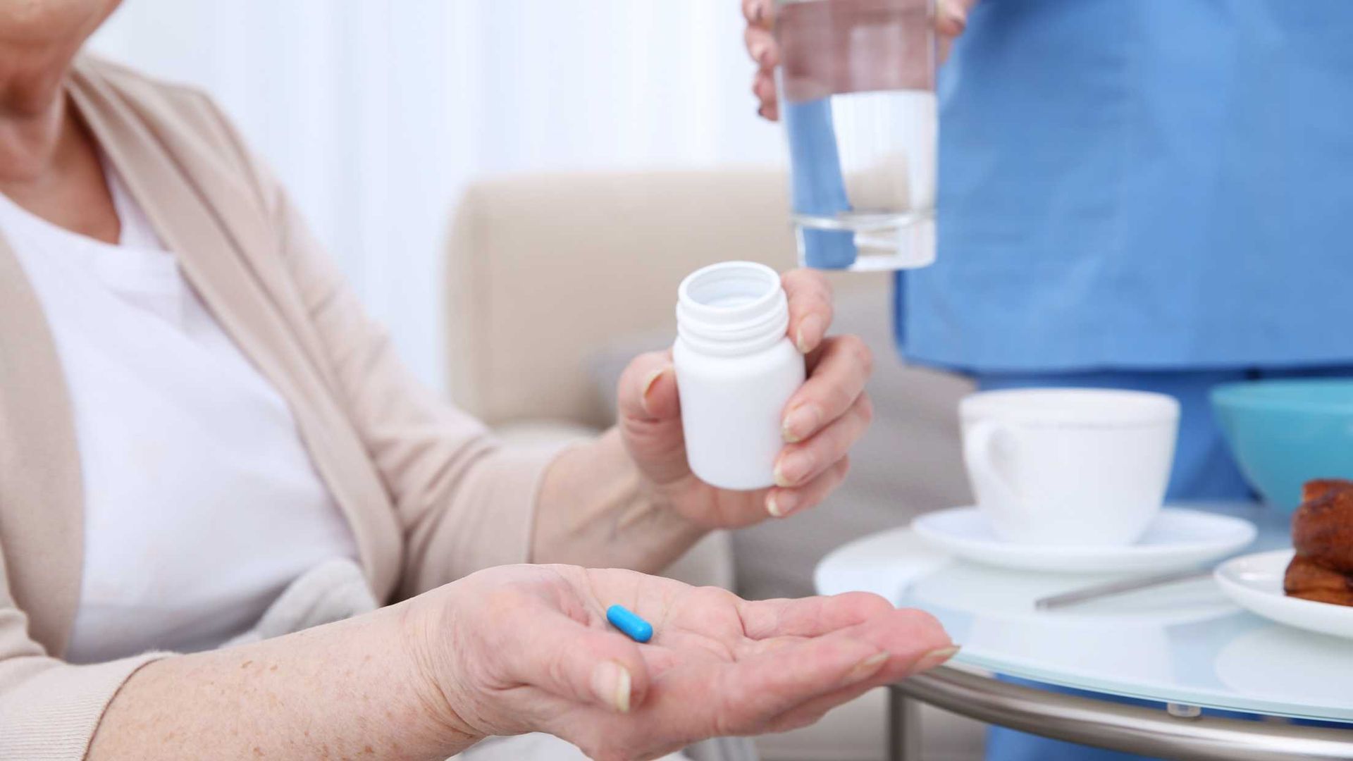 An elderly woman is holding a bottle of pills and a glass of water.