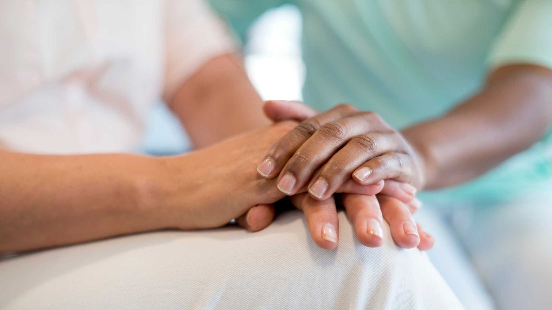 A nurse is holding the hand of a patient in a hospital bed.
