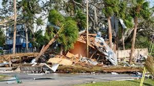 Hurricane damage: Debris, fallen trees, and a destroyed building. A roadway is in the foreground.