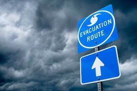 Blue evacuation route sign with arrow against a stormy sky.