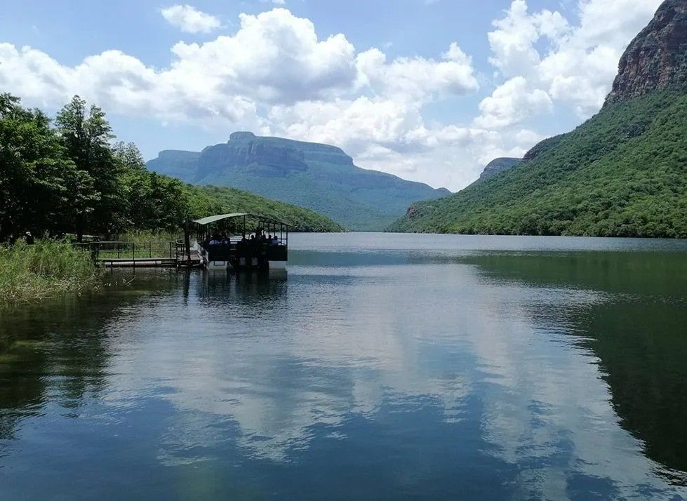 Calm lake with mountain cliffs, blue sky, and a small dock on the left shoreline