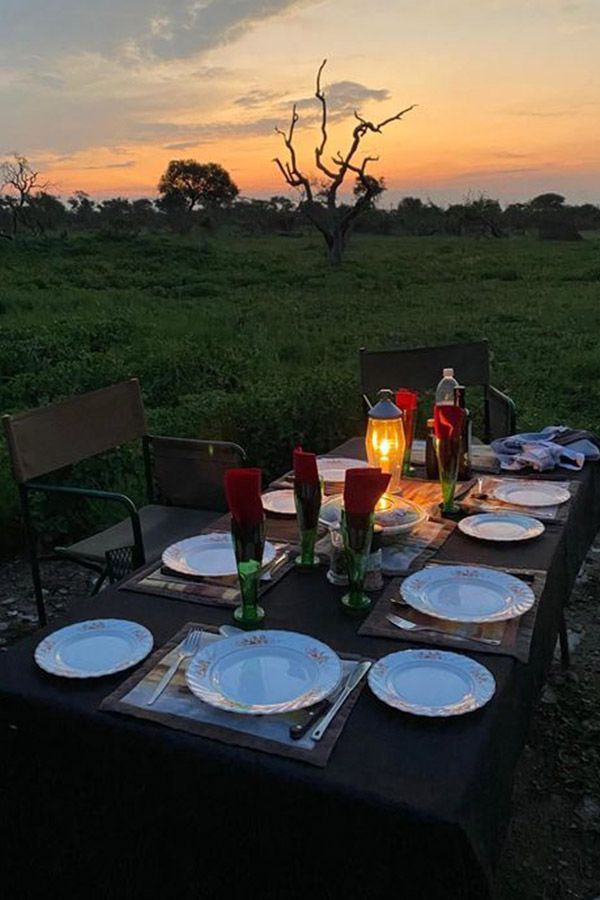 Outdoor table set for dinner at sunset, with plates, glasses, and a lantern.