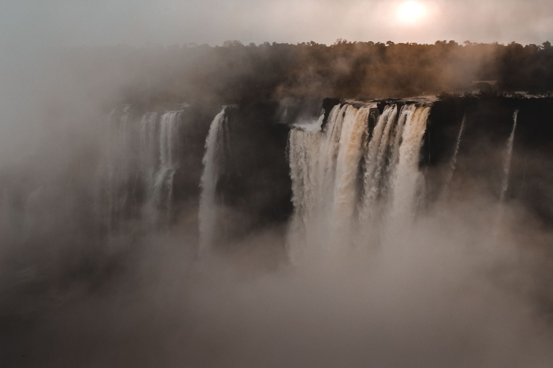 Mist-covered waterfall at sunrise, with golden light over a forested cliff.