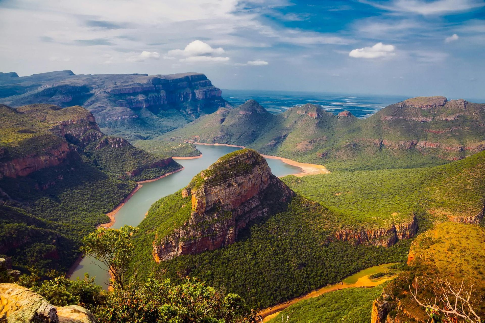 Wide river winding through lush green canyon cliffs under a bright sky