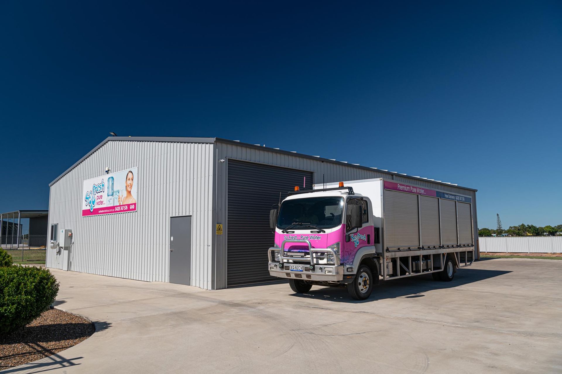 Pink-and-grey truck parked beside a large metal warehouse under a clear blue sky — So Fresh Wide Bay in Burnett Heads, QLD