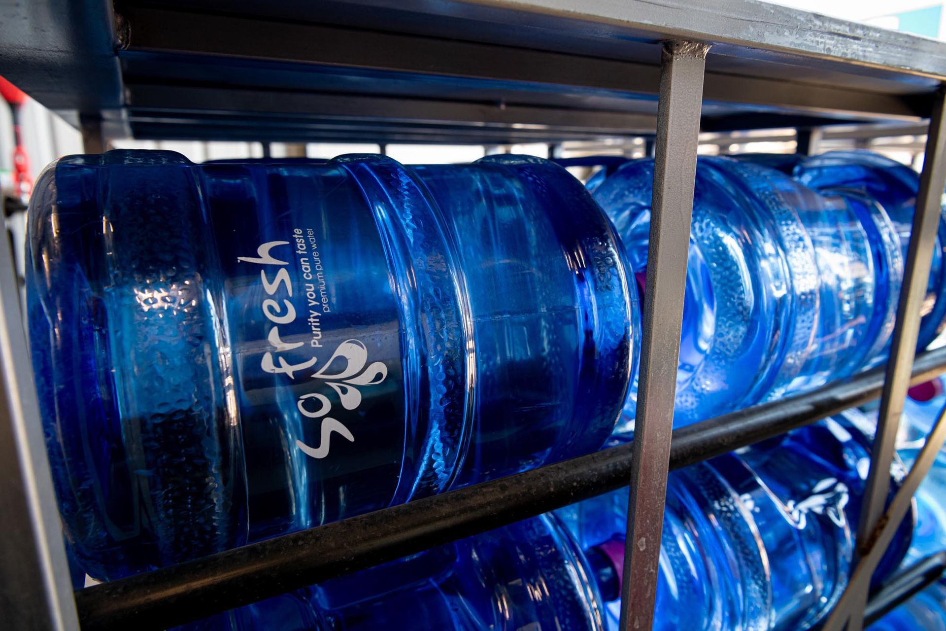 Blue water jugs stacked on metal racks in a storage area — So Fresh Wide Bay in Moore Park, NSW