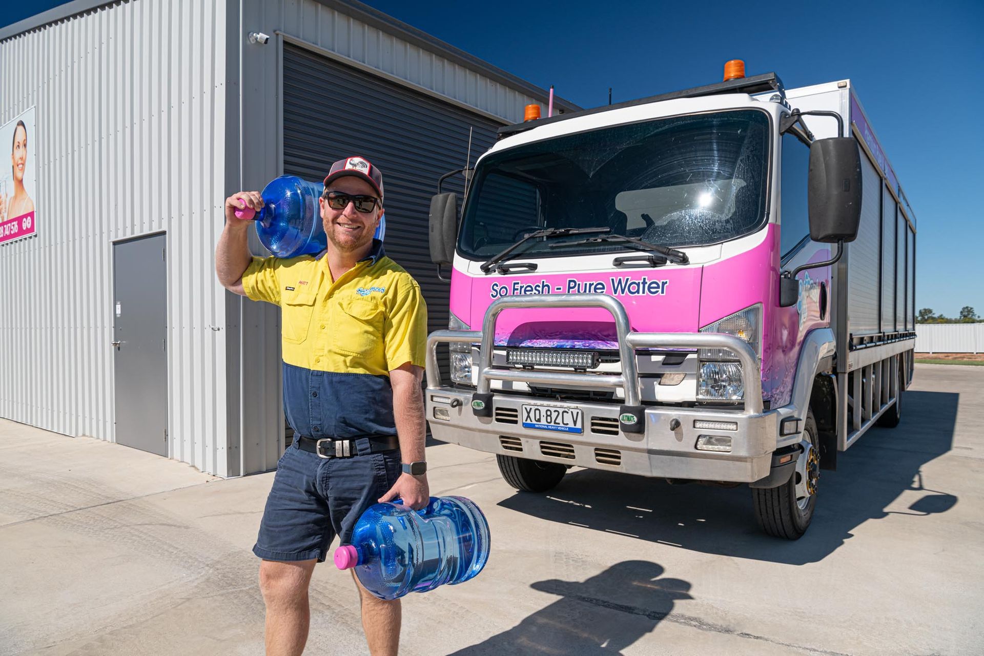 Person in yellow shirt holding water jugs beside a pink truck outside a warehouse — So Fresh Wide Bay in Innes Park, QLD