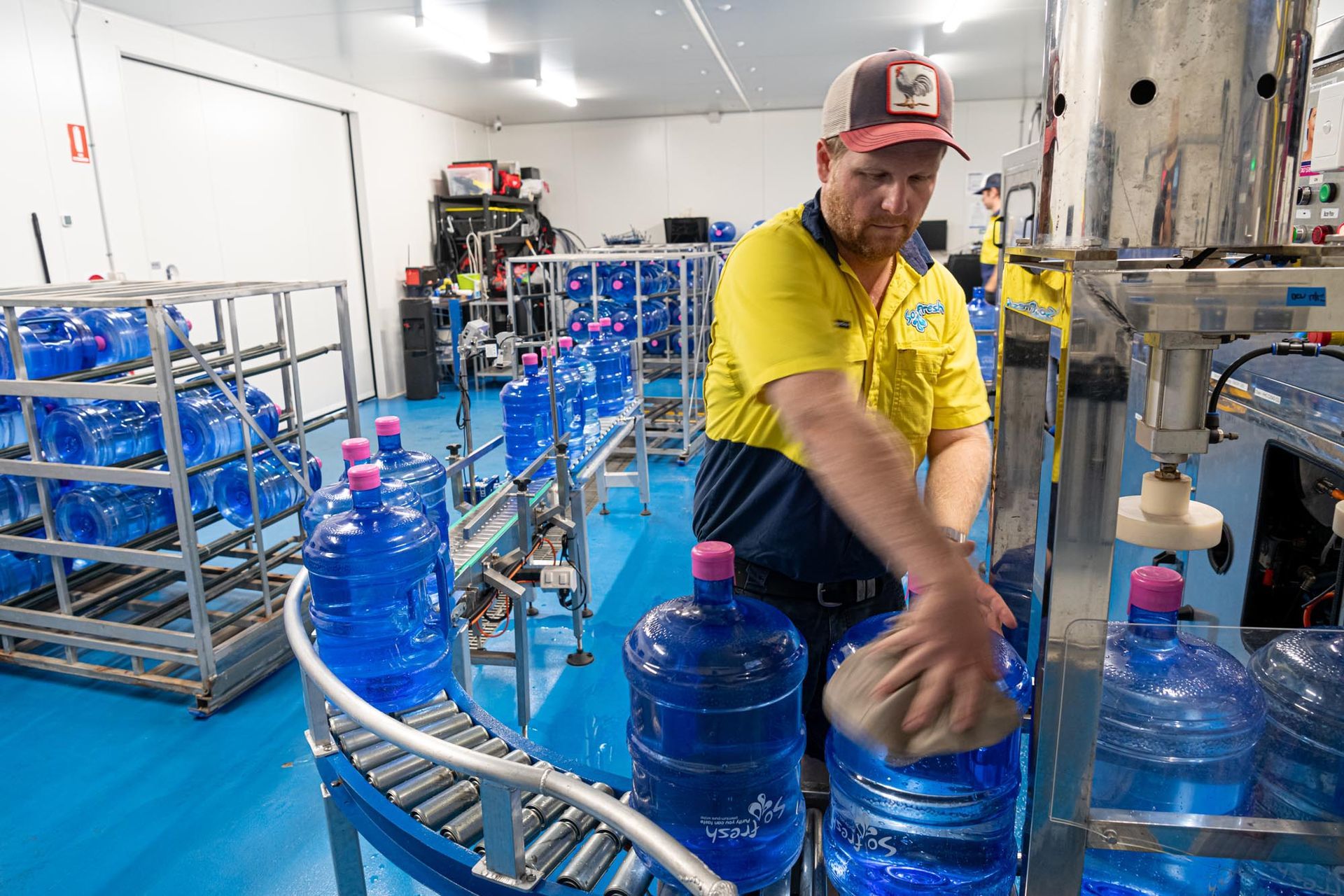 Worker in a yellow shirt filling large blue water jugs on a factory conveyor line — So Fresh Wide Bay in Burnett Heads, QLD
