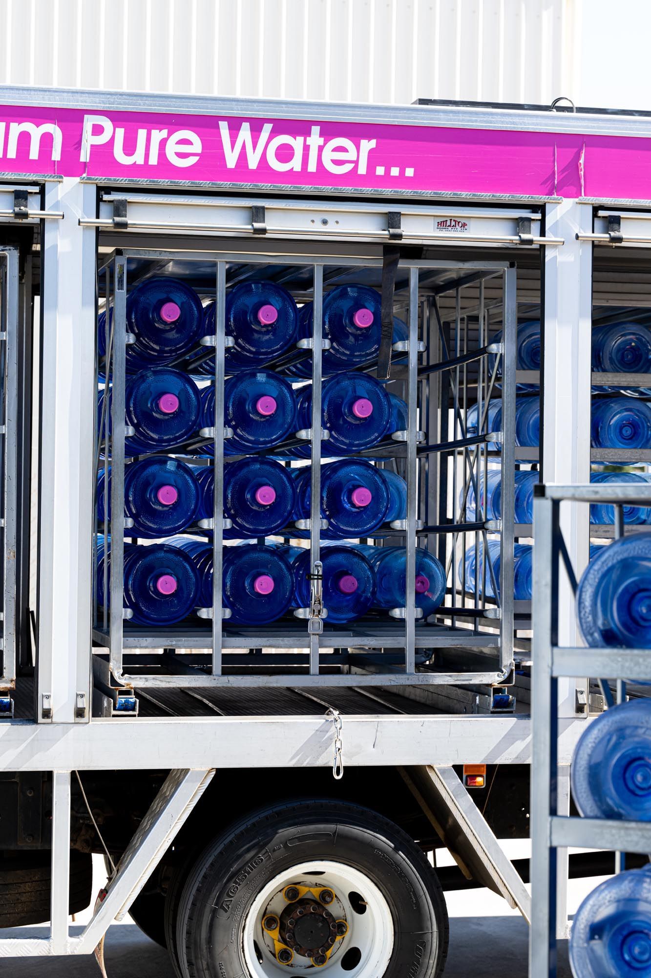 Truck Loaded With Blue Water Jugs in a Rack, Under a Sign Reading “pure Water” — So Fresh Wide Bay in Thabeban, QLD