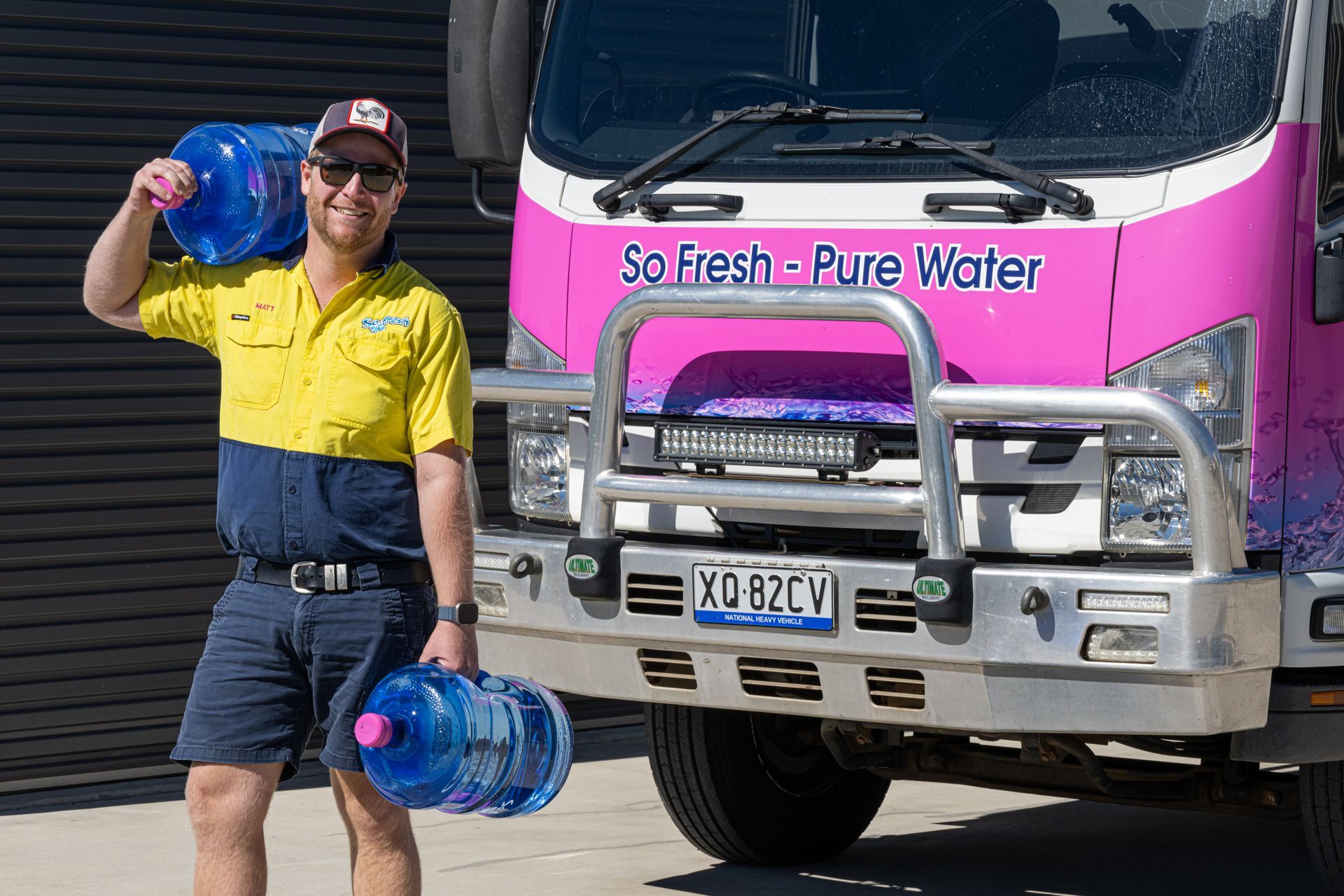 Delivery worker holding large water bottles in front of a pink “So Fresh + Pure Water” truck — So Fresh Wide Bay in Thabeban, QLD