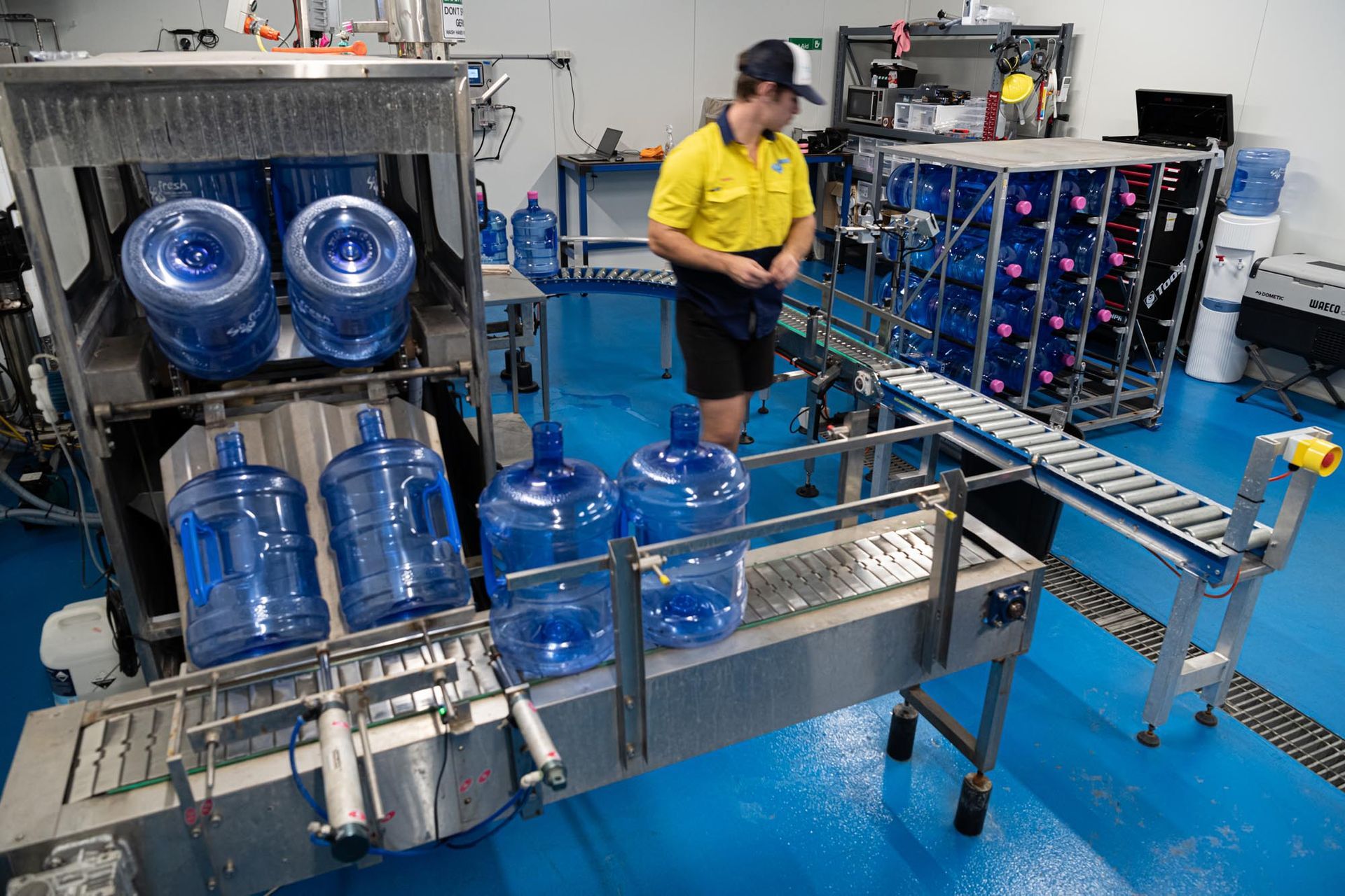 Water bottling line with blue 5-gallon jugs and a worker in a yellow shirt in a factory — So Fresh Wide Bay in Childers, QLD