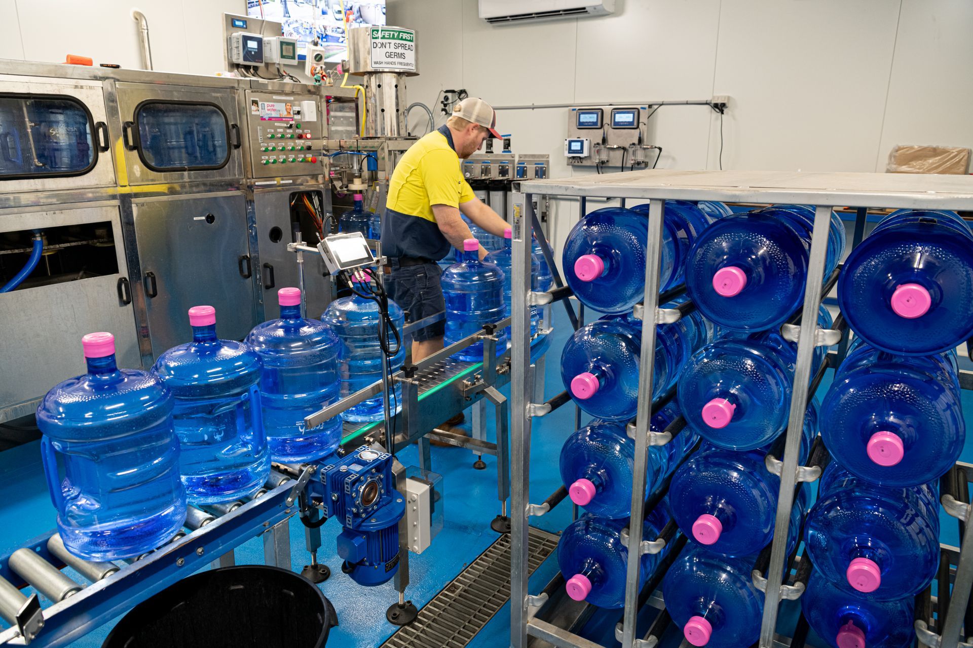 Worker in a bottling plant beside stacks of blue water jugs and industrial equipment