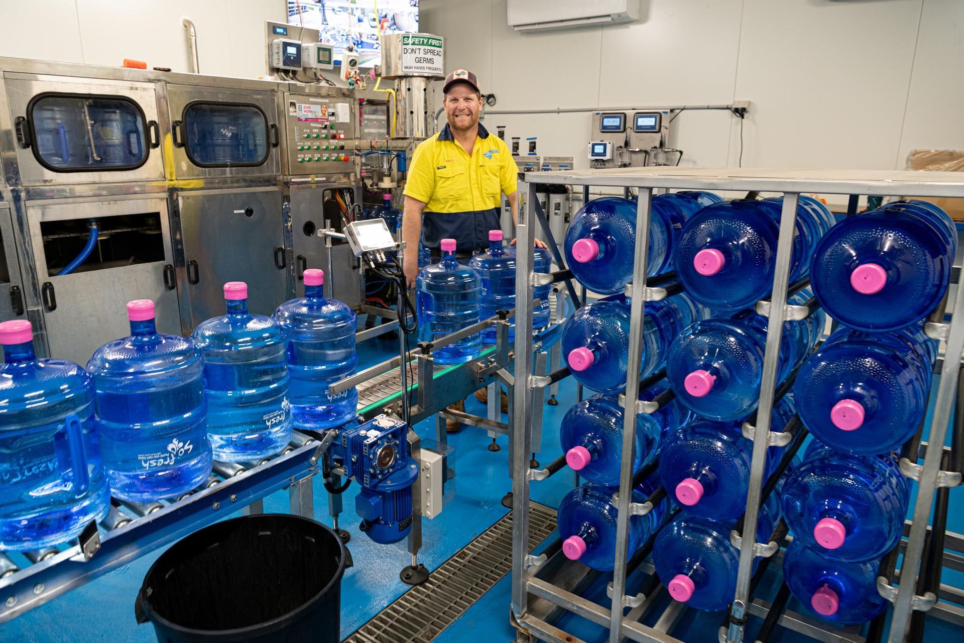 Water bottling facility with large blue bottles on conveyor belts and a worker in a yellow uniform — So Fresh Wide Bay in Moore Park, NSW