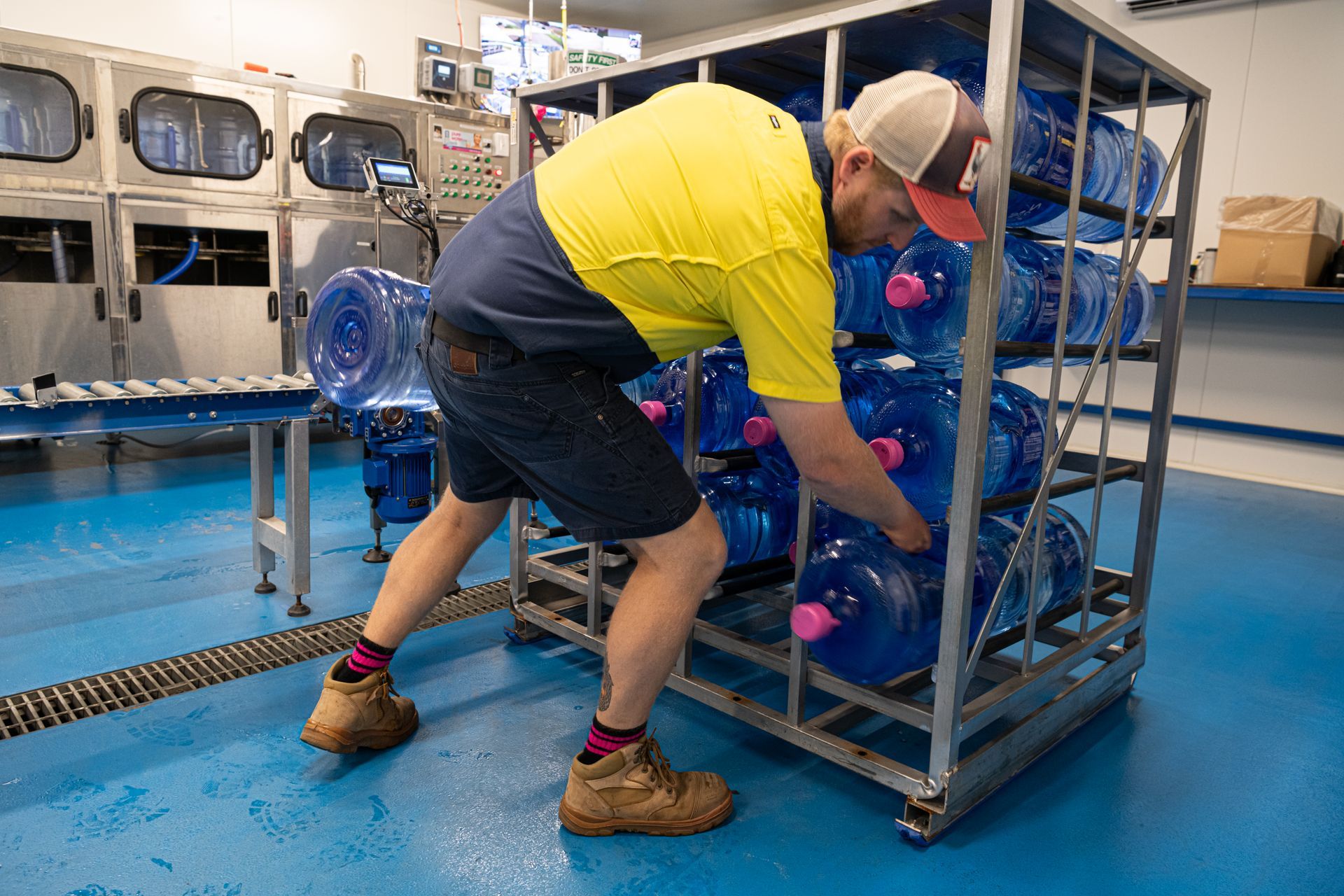 Worker in yellow shirt loading blue water jugs onto a metal cart in a laundromat-like room — So Fresh Wide Bay in Burnett Heads, QLD