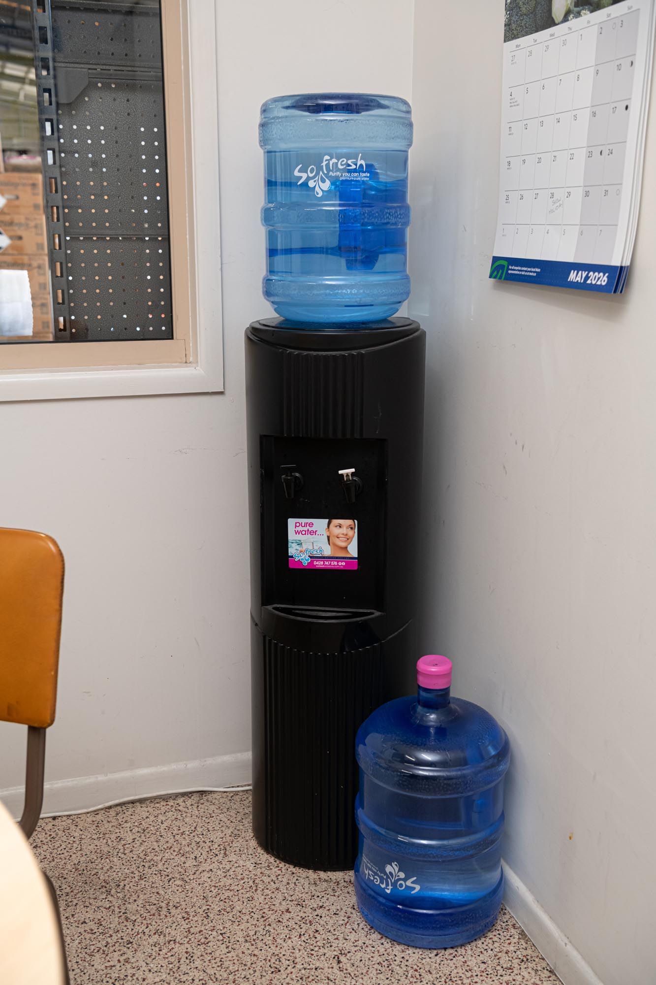 Water cooler with blue jugs in an office corner, next to a wall calendar and window — So Fresh Wide Bay in Thabeban, QLD