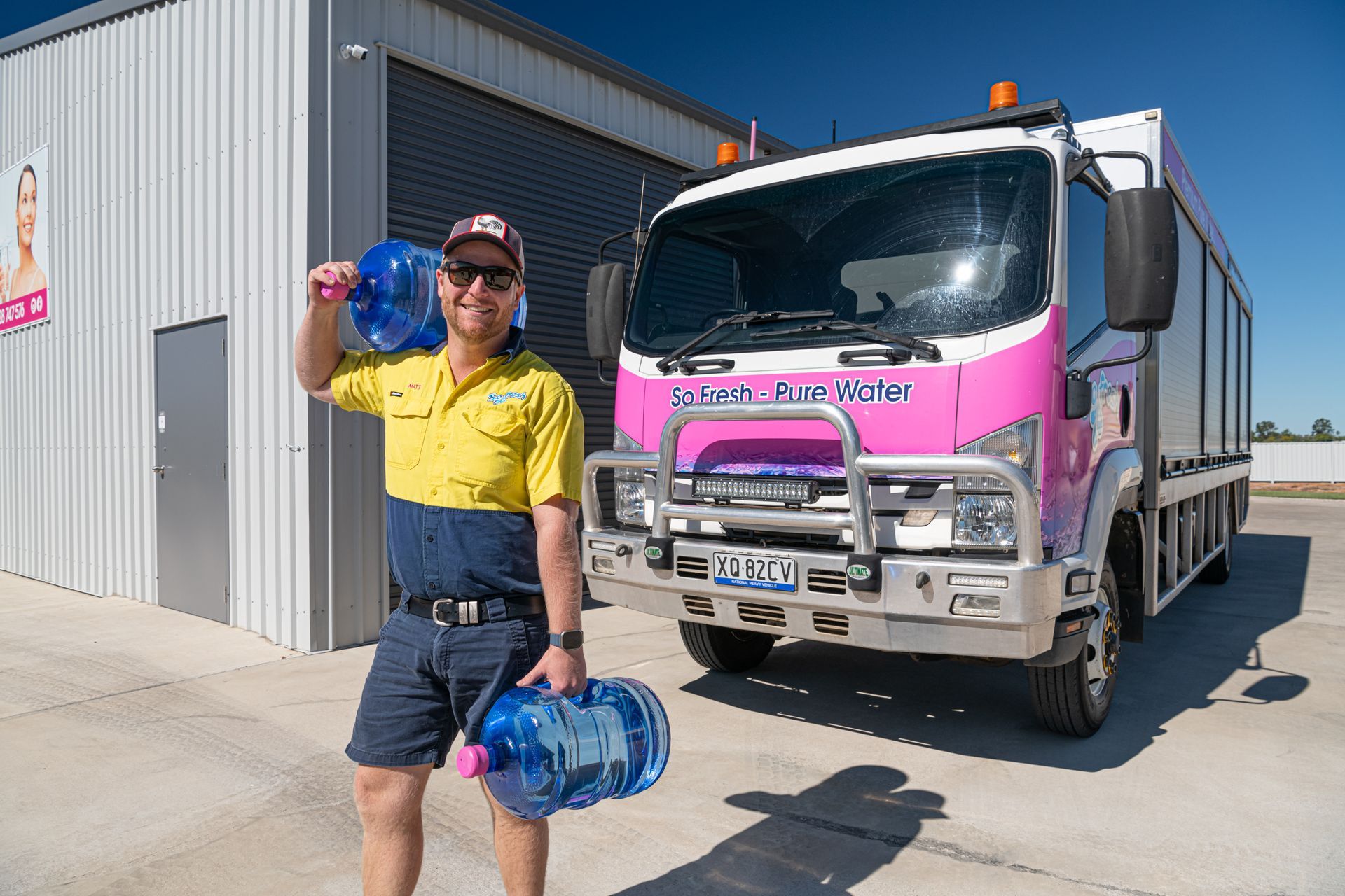 Worker holding blue bottles beside a pink truck outside a warehouse