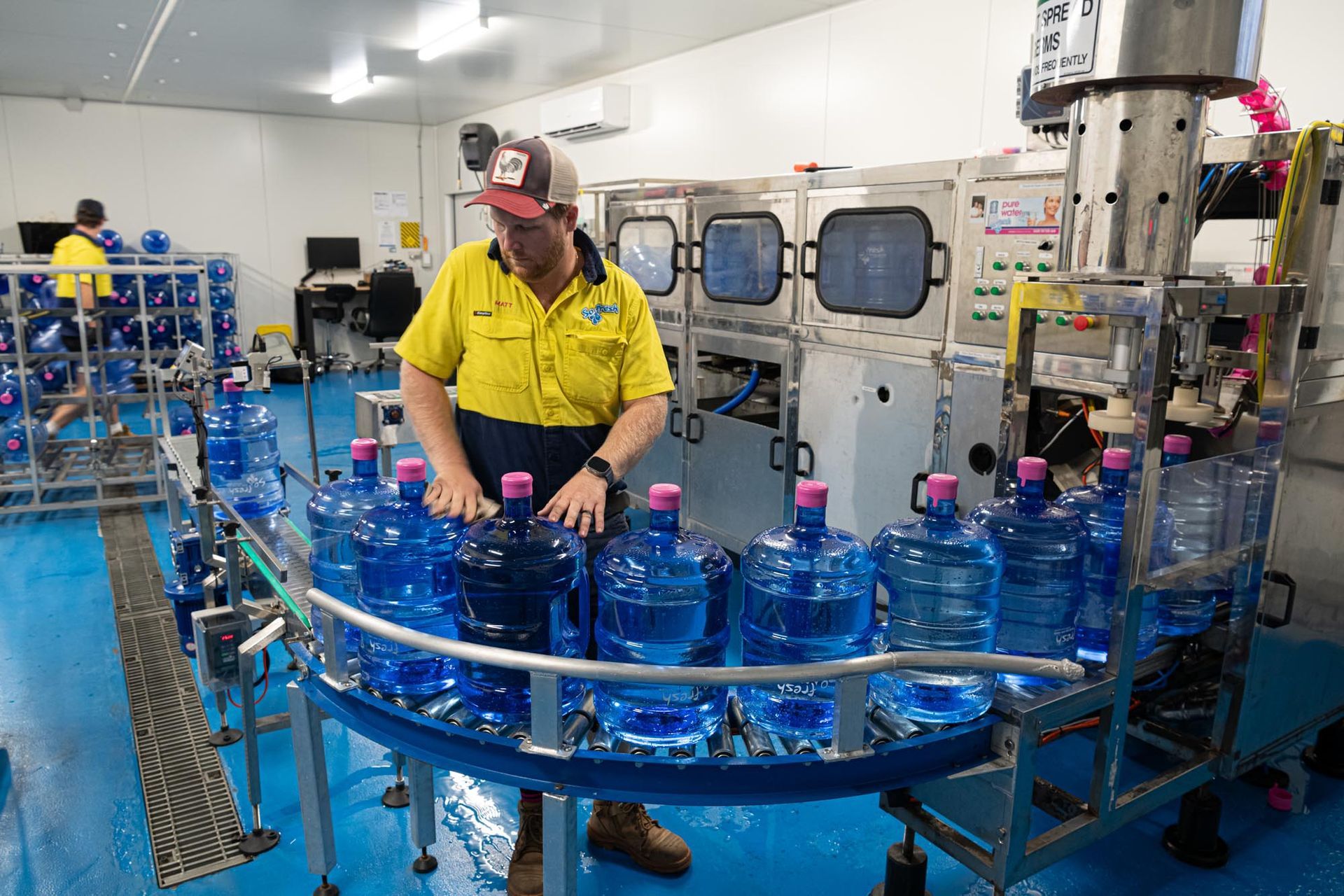 Worker in yellow shirt operating bottling machine beside rows of blue water bottles in a factory — So Fresh Wide Bay in Thabeban, QLD
