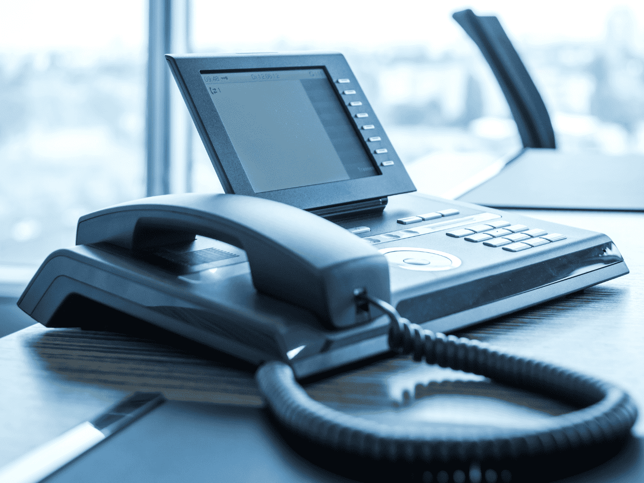 A telephone is sitting on a desk in front of a window