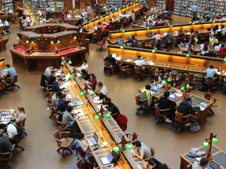 A group of people are sitting at long tables in a library.