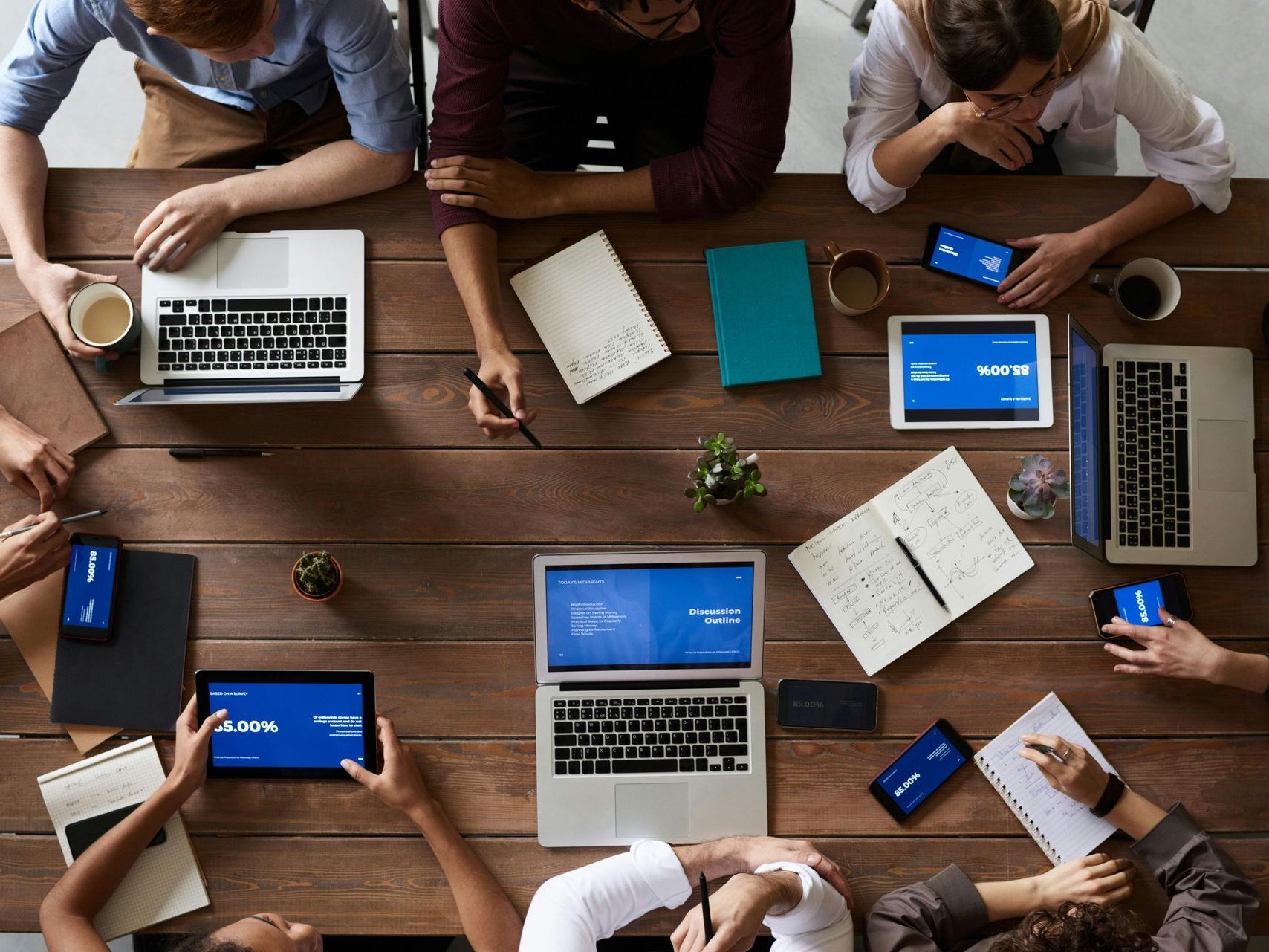 A group of people are sitting around a table with laptops and tablets.