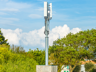 A cell phone tower is sitting in the middle of a field surrounded by trees.