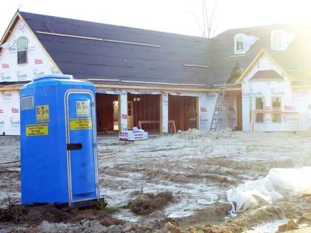Blue portable toilet in front of a house under construction.