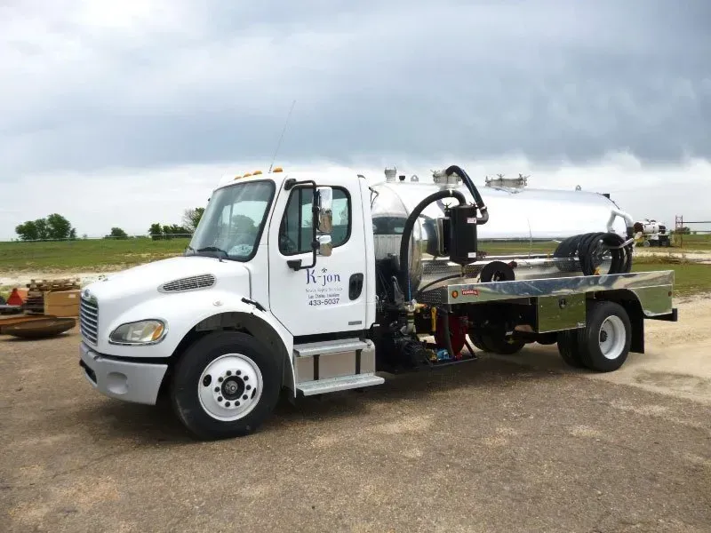 White sanitation truck with silver tank on a flatbed, parked outdoors under a cloudy sky.