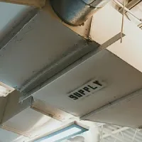 A white rectangular HVAC supply duct hangs from a ceiling, with the word 