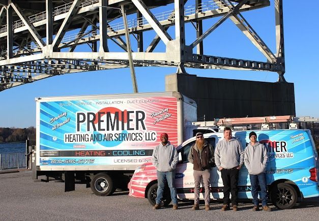 Four people stand before a box truck and a service van branded with the Premier Heating and Air Services LLC logo.