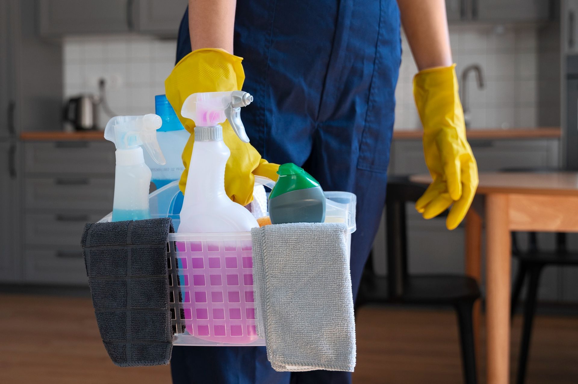 Persona que sostiene productos de limpieza en un carrito, con guantes amarillos, en una cocina.