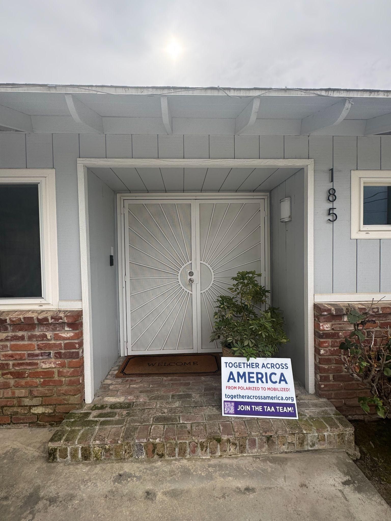 Front entrance of a house with light grey siding, decorative white double doors, and a political sign on the steps.