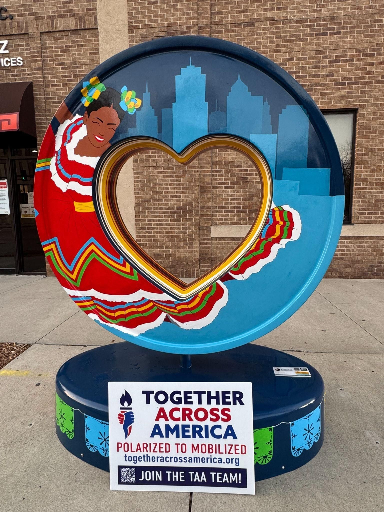 A blue circular sculpture with a central heart cutout, featuring a dancer and city skyline, with a