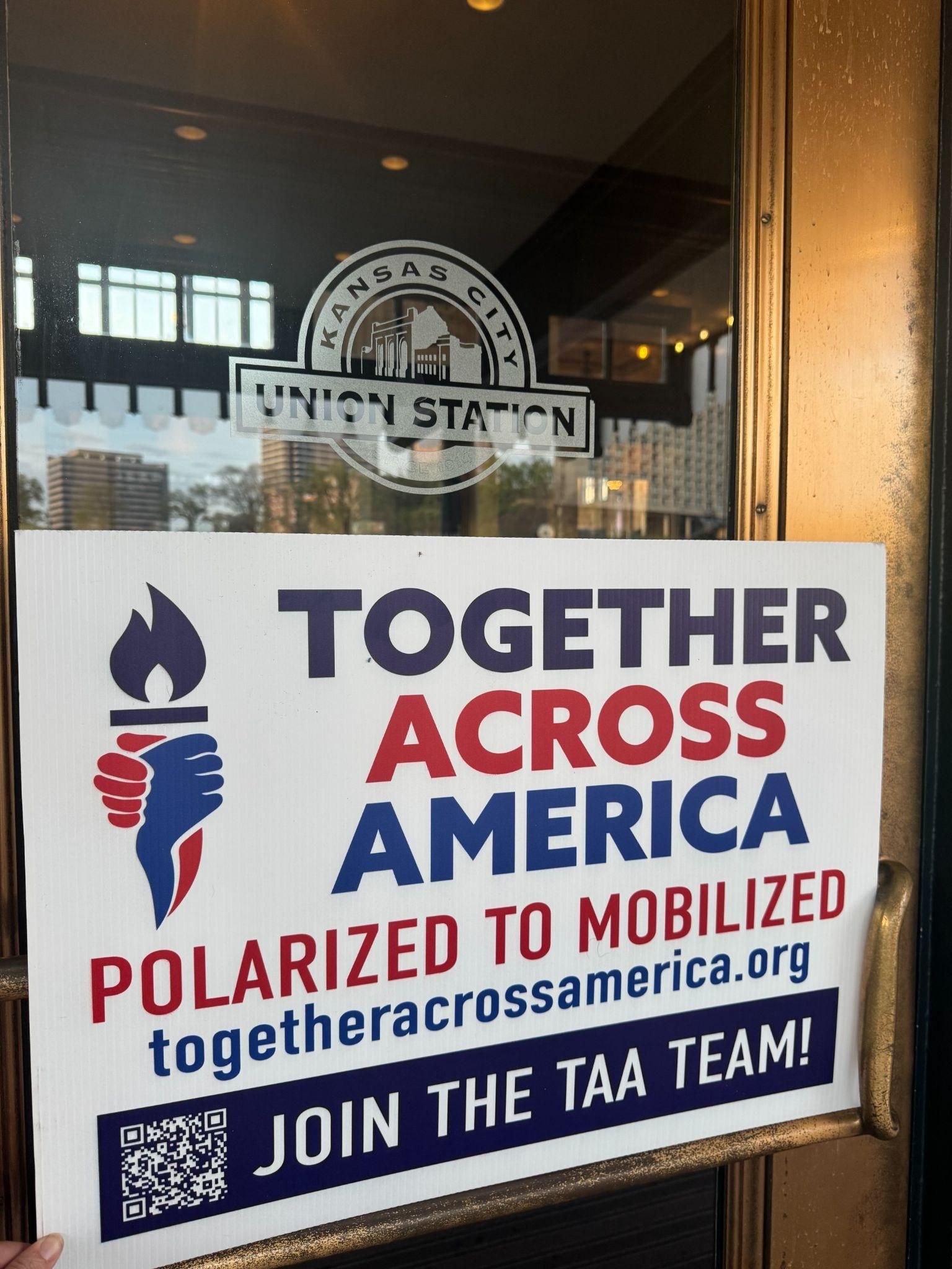 A flyer for Together Across America posted on a glass door at Kansas City Union Station, including a QR code to join.
