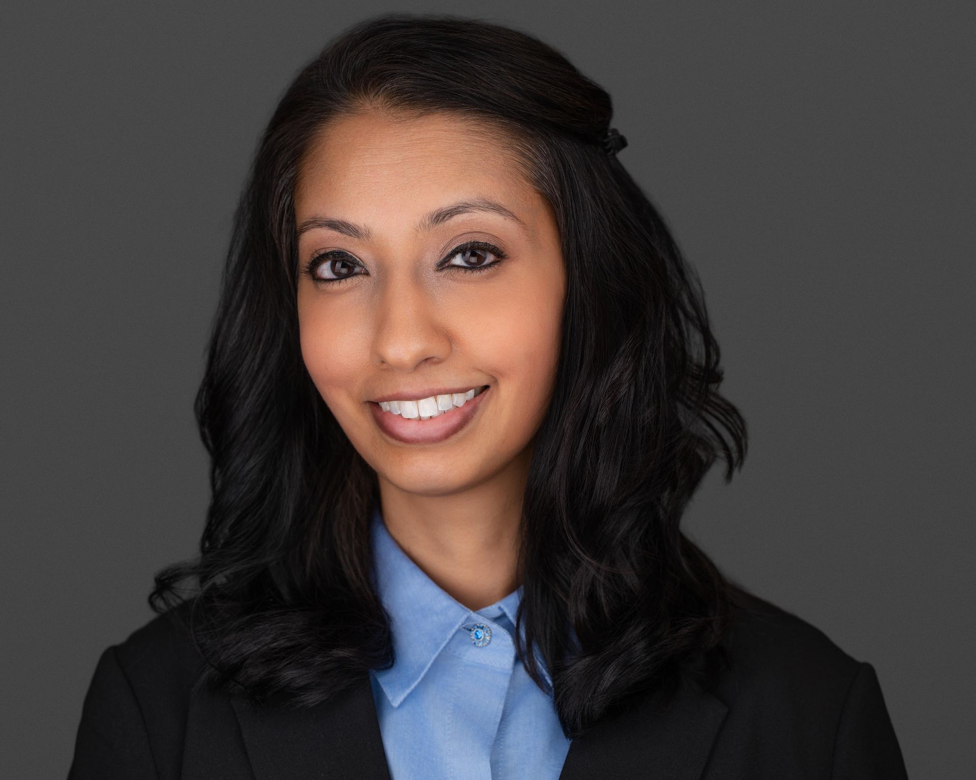 A woman wearing a white lab coat and a black shirt is smiling for the camera.