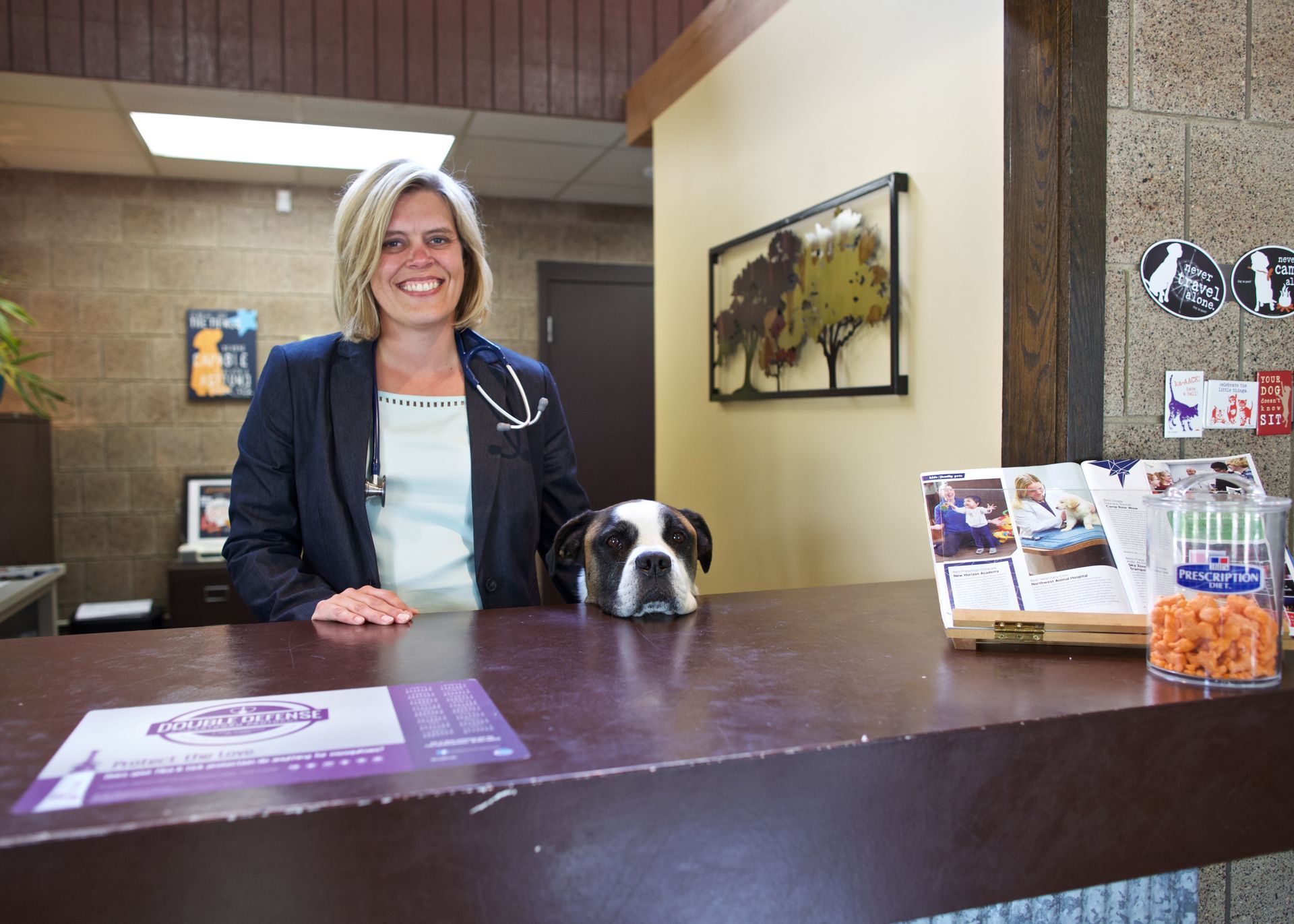 Woman behind reception desk with a dog beside her and brochures on the counter