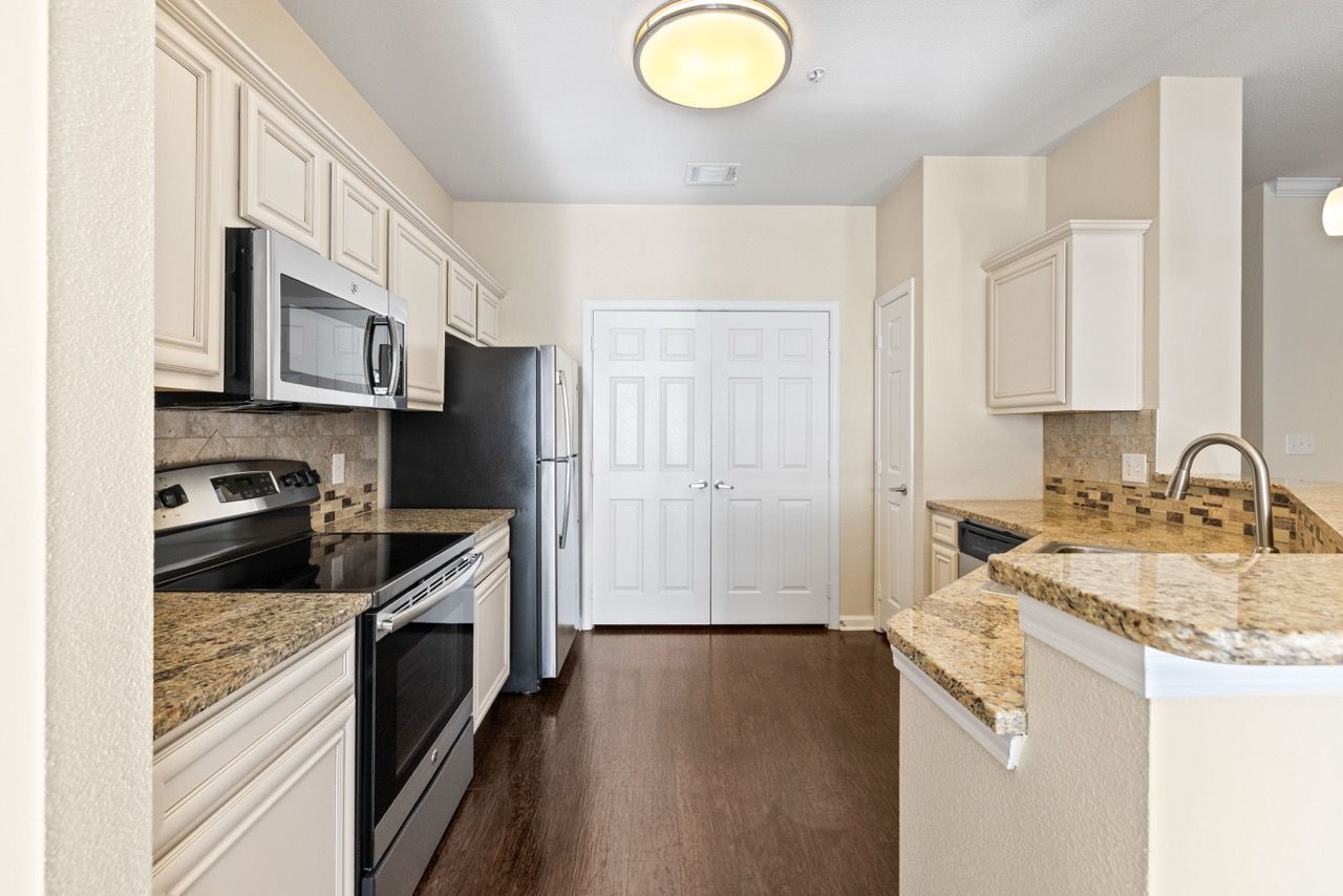 Modern apartment kitchen with granite countertops, white cabinets, and stainless steel appliances.