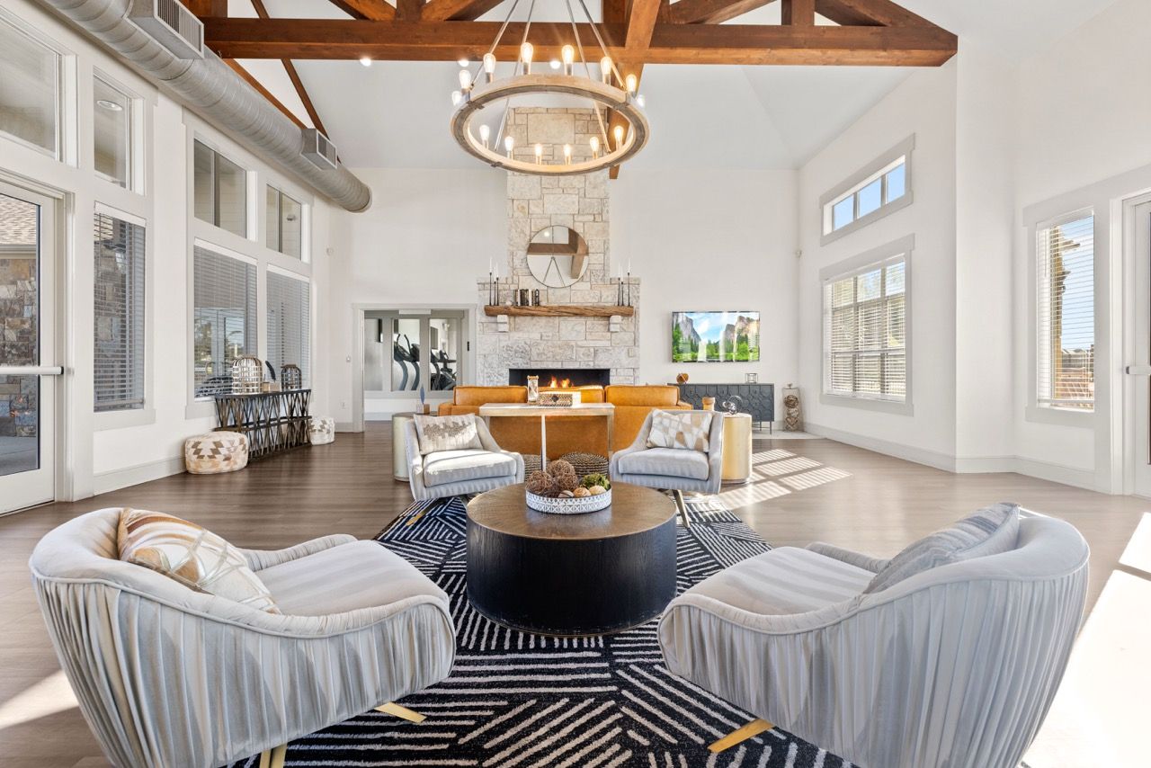 Bright modern living room with a stone fireplace, exposed wood beams, and large windows.