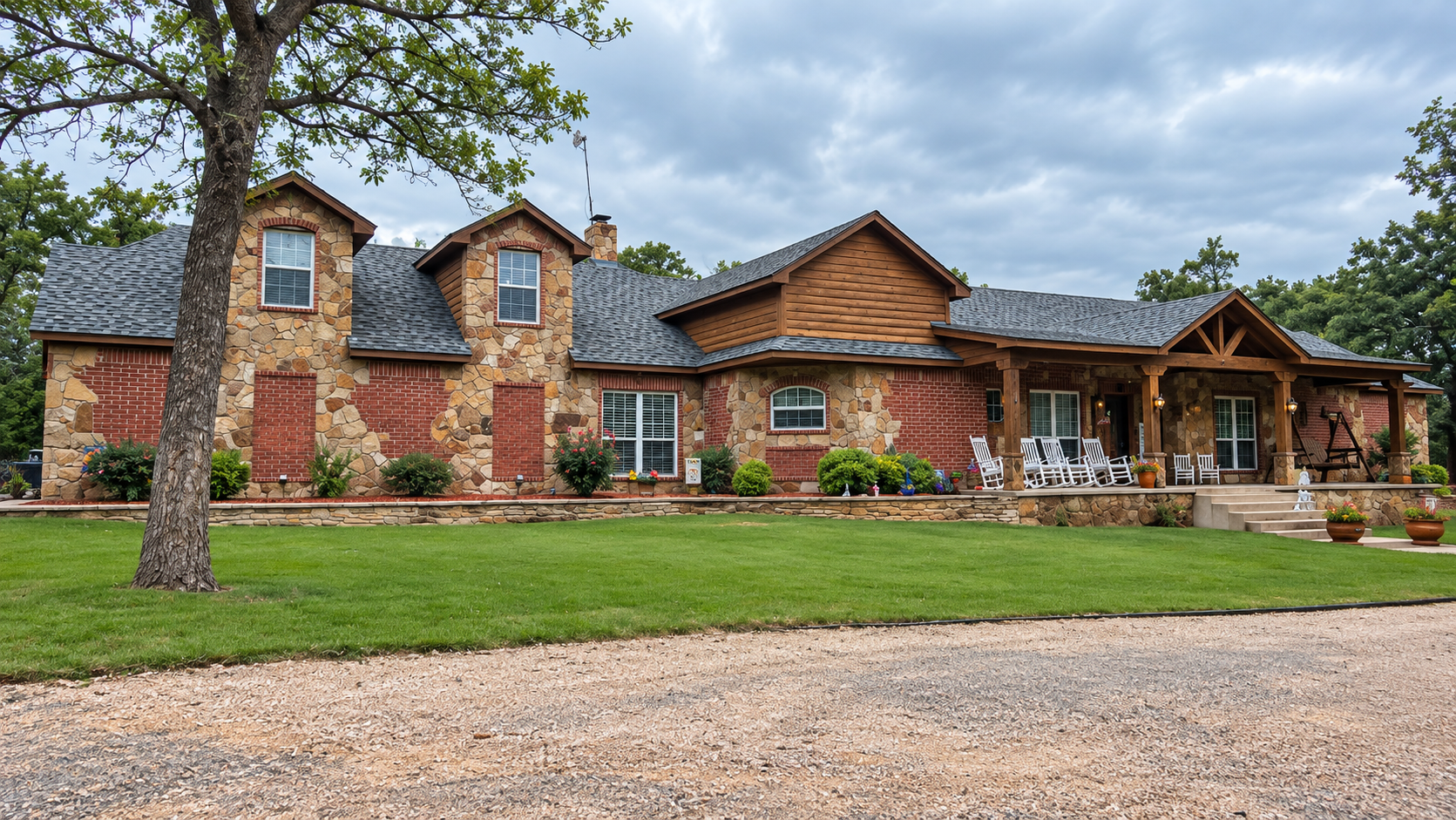 Stone ranch-style house with red brick, wood siding, and a large front porch behind a green lawn