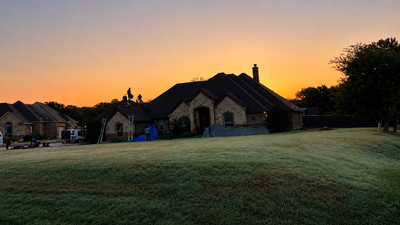 Houses silhouetted at sunset over a frosty grassy field under an orange sky