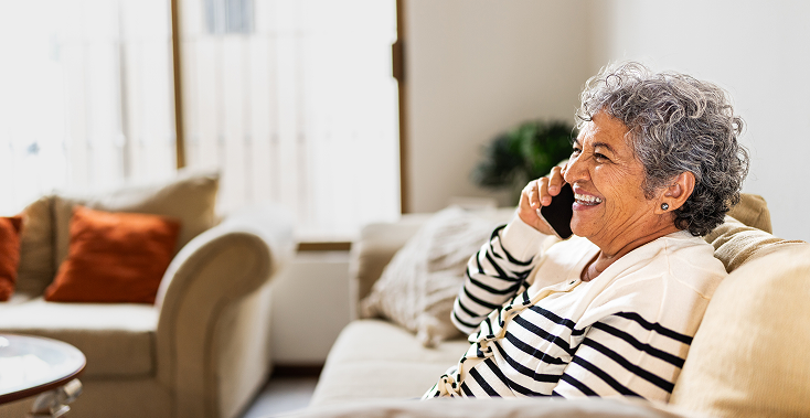 Woman on sofa smiling while talking on a phone indoors.