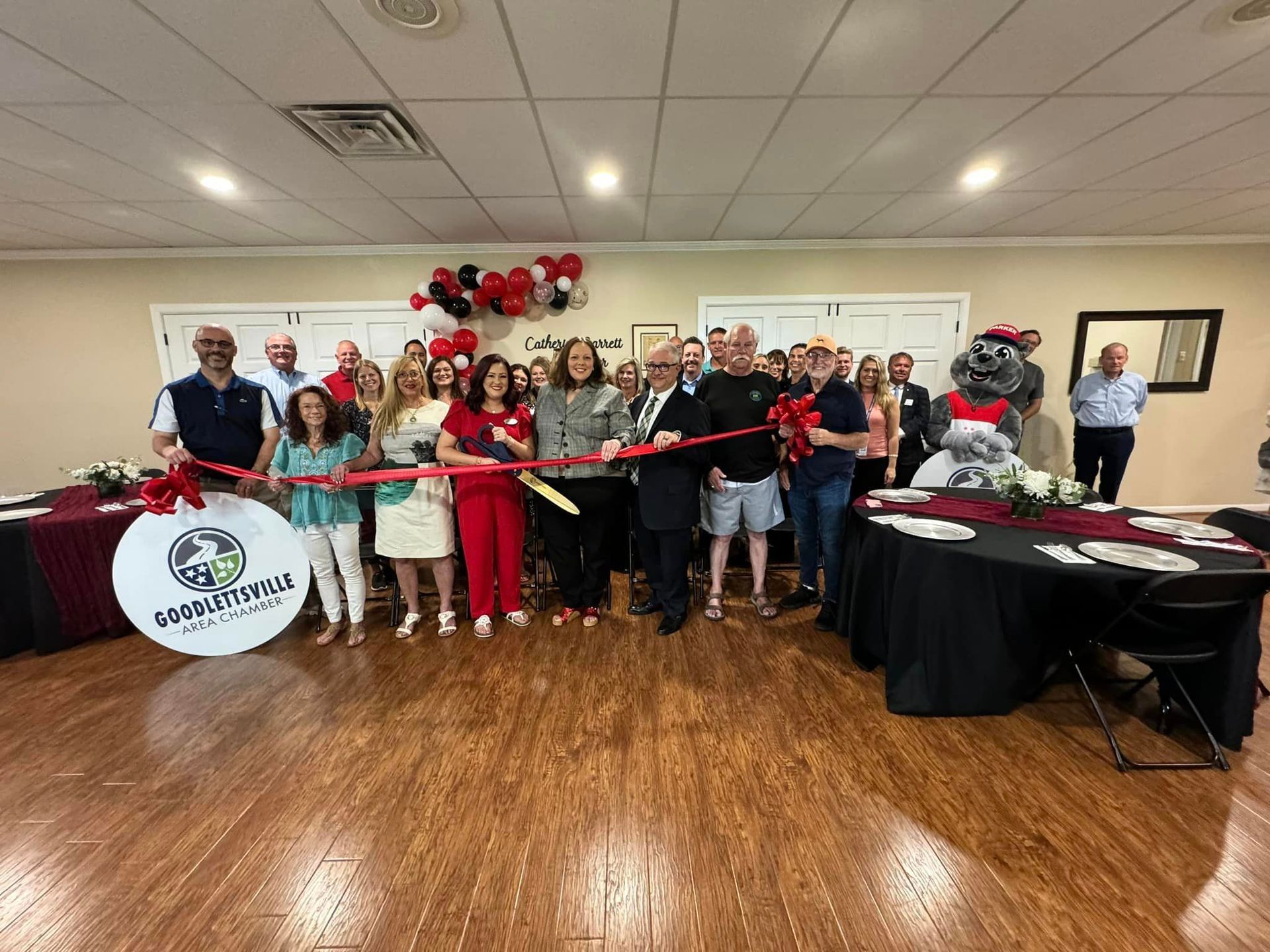 A group of people are standing in a room cutting a red ribbon.