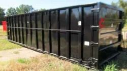 Black metal dumpster or waste container outdoors on grass, side view